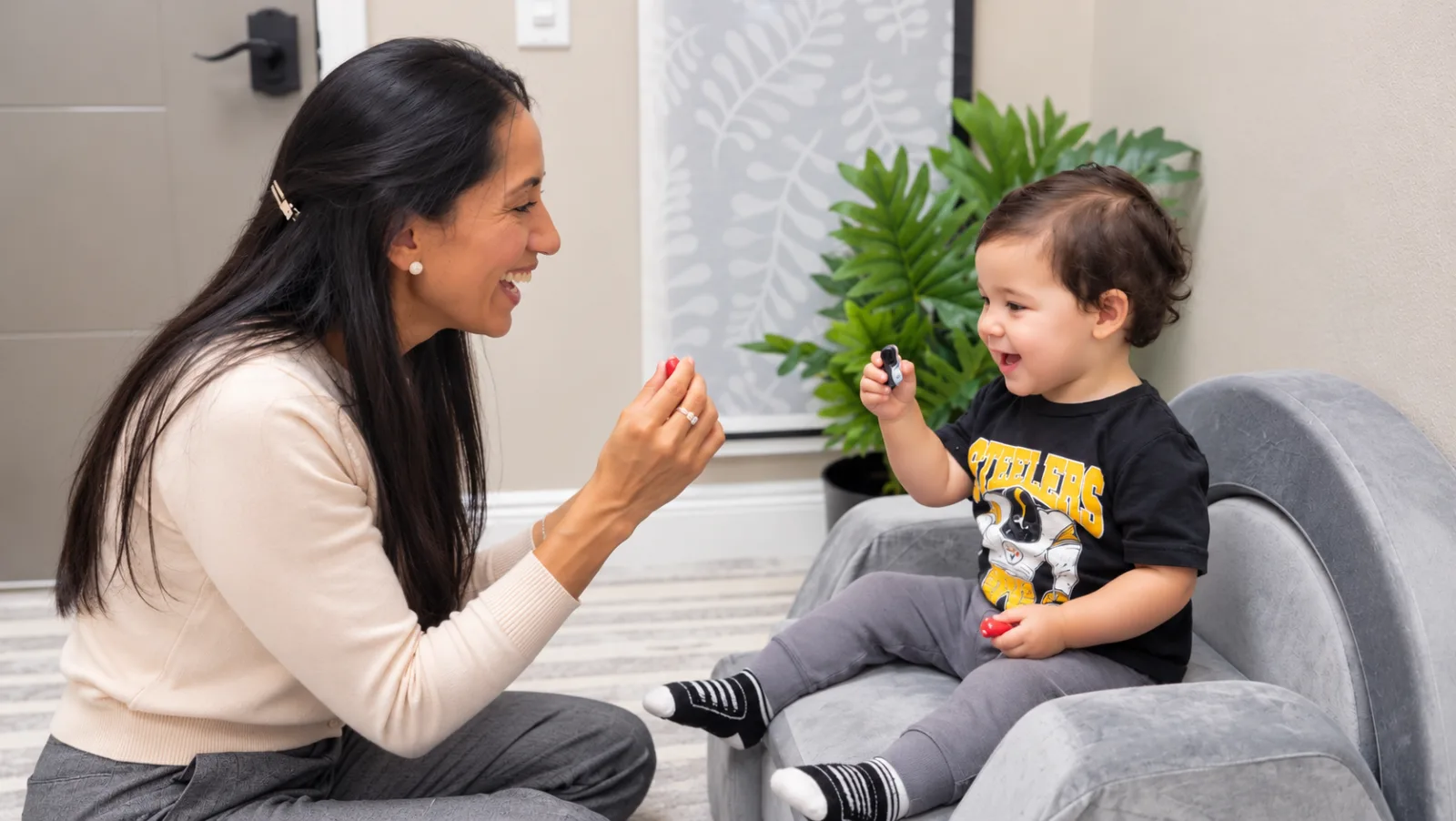 Karin and a laughing toddler holding up small toys to each other during a play-based session